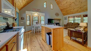 A spacious kitchen with a wooden ceiling, a dining area with a table and chairs, a living room with a couch and a TV, and a sign indicating a bait shop.