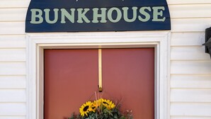A red door with a 'COUNTRY BUNKHOUSE' sign above it and a hanging flower basket.