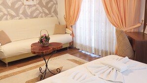 A hotel room with a bed, a sofa, a small round table with a vase of flowers, and a large window with curtains. - Jasmin Apart Hotel (Fethiye)