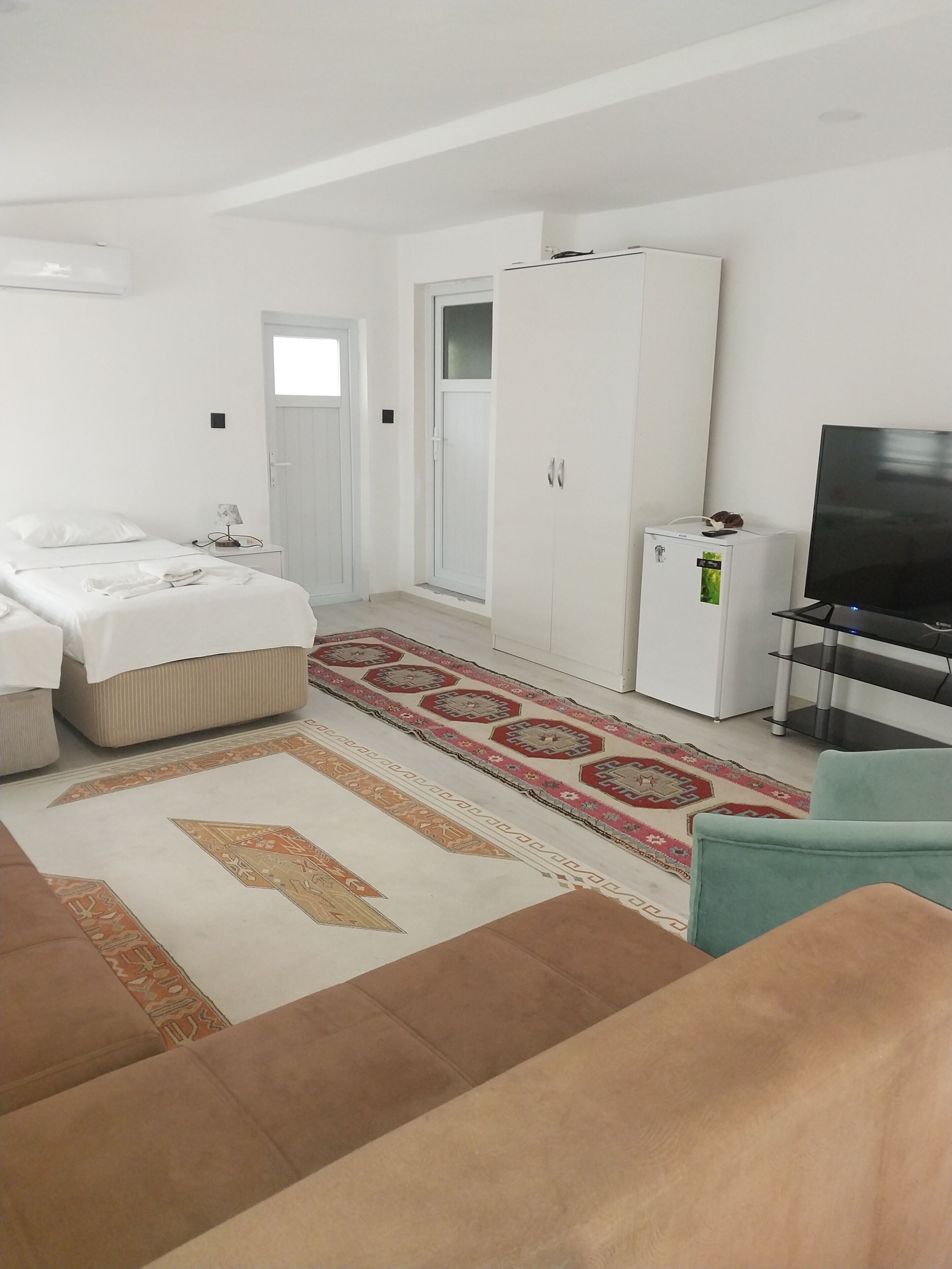 Una habitación de hotel con cama, armario, televisión y un refrigerador pequeño.