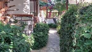 A stone pathway flanked by dense green hedges leading to a building with a wooden roof and a stone wall. - Jasmin Apart Hotel (Fethiye)