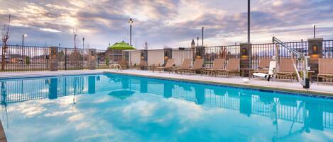 A clear blue pool with lounge chairs and a fence, surrounded by a cloudy sky.