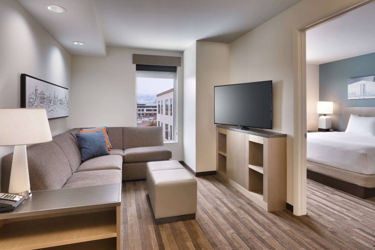 Ein modernes Hotelzimmer mit einer Couch, einem Flachbildfernseher, einem Bett und einem Schreibtisch mit einer Lampe.
