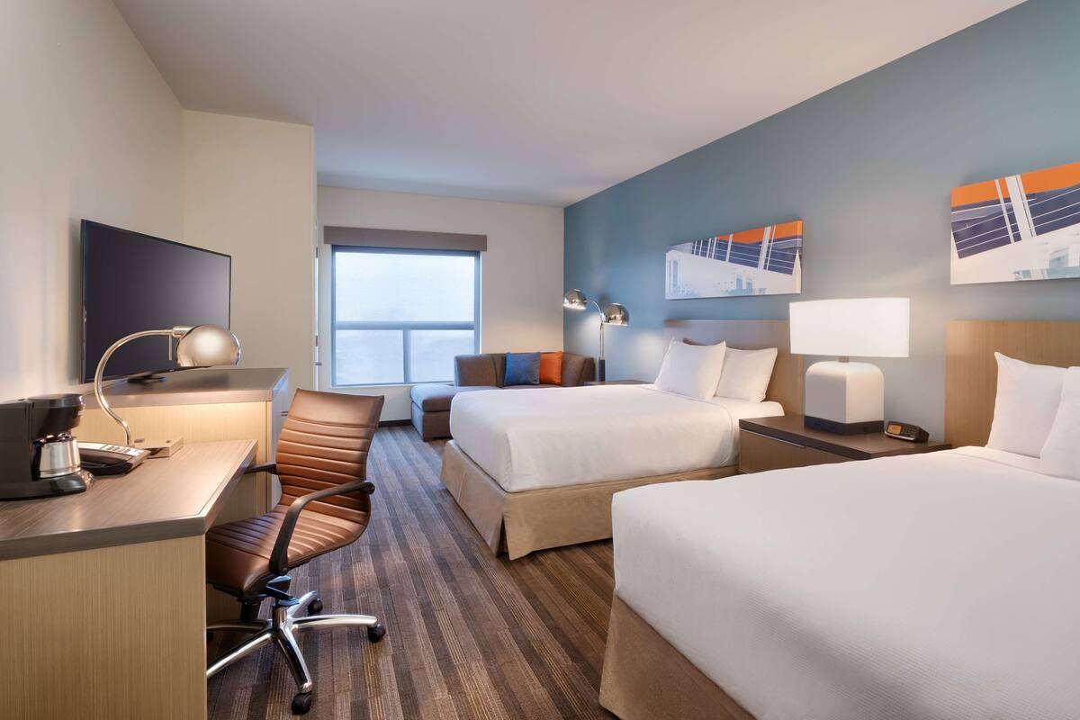 Ein Hotelzimmer mit zwei Betten, einem Schreibtisch mit Computer, einem Stuhl und einem Fenster.