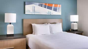 Habitación de hotel con cama, dos mesitas de noche con lámparas, una mesita de noche con un reloj y un cuadro abstracto colgado en la pared.