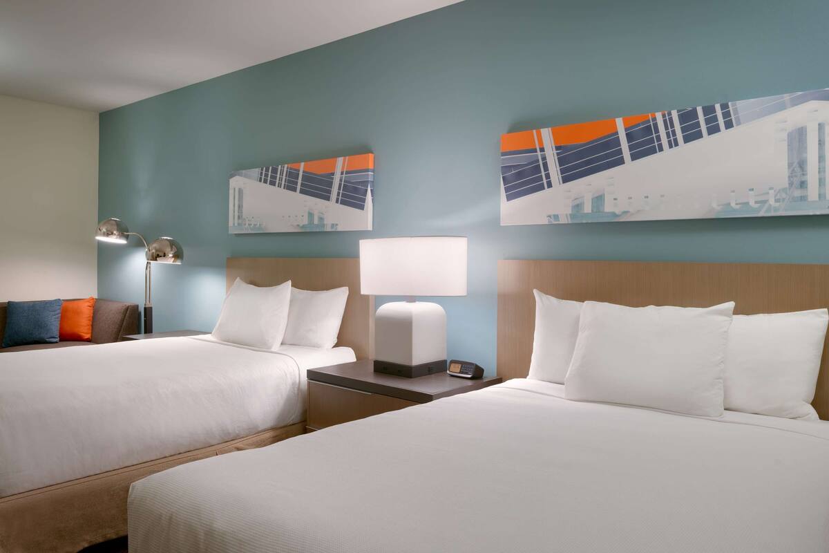 Ein Hotelzimmer mit zwei Betten, einem Nachttisch mit Lampe und zwei Wandbildern.