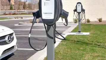 Uma estação de carregamento para veículos elétricos com identificação de estação de alta potência, localizada em um estacionamento com um edifício ao fundo.