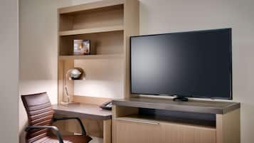 Une chambre d’hôtel moderne dotée d’un bureau en bois, d’un fauteuil en cuir, d’un téléviseur à écran plat et d’étagères intégrées.