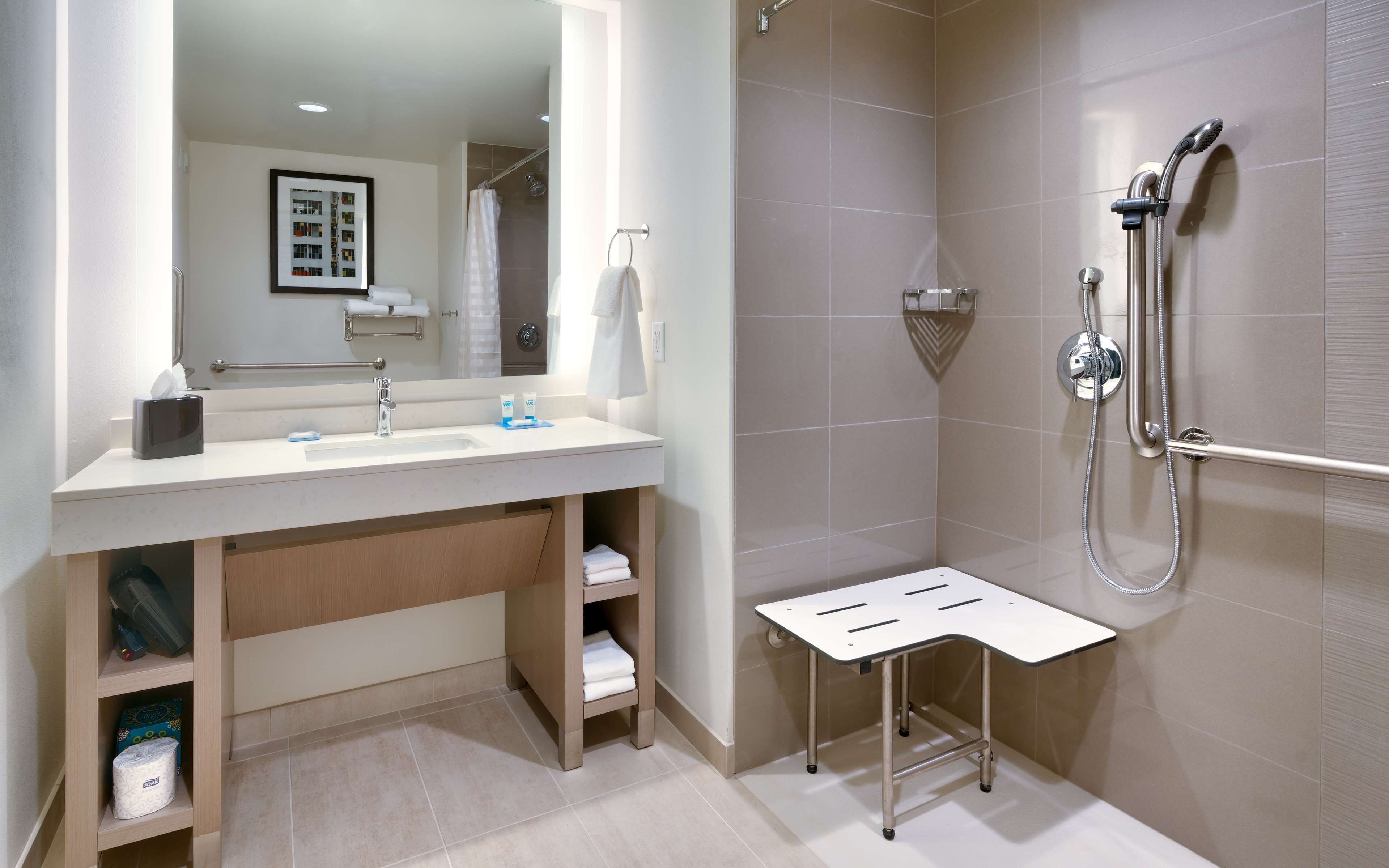 Un baño moderno con lavamanos, espejo, toallero y ducha.