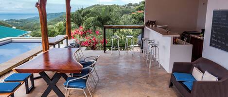 A covered outdoor area with a pool, seating, and a bar.