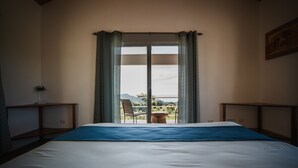 Habitación de hotel con una cama grande, vistas al exterior a través de una puerta corrediza, una silla y una mesita.