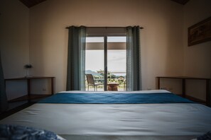A hotel room with a large bed, a view of the outdoors through a sliding door, a chair, and a small table. - Lodge Las Estrellas de Samara (Sámara)