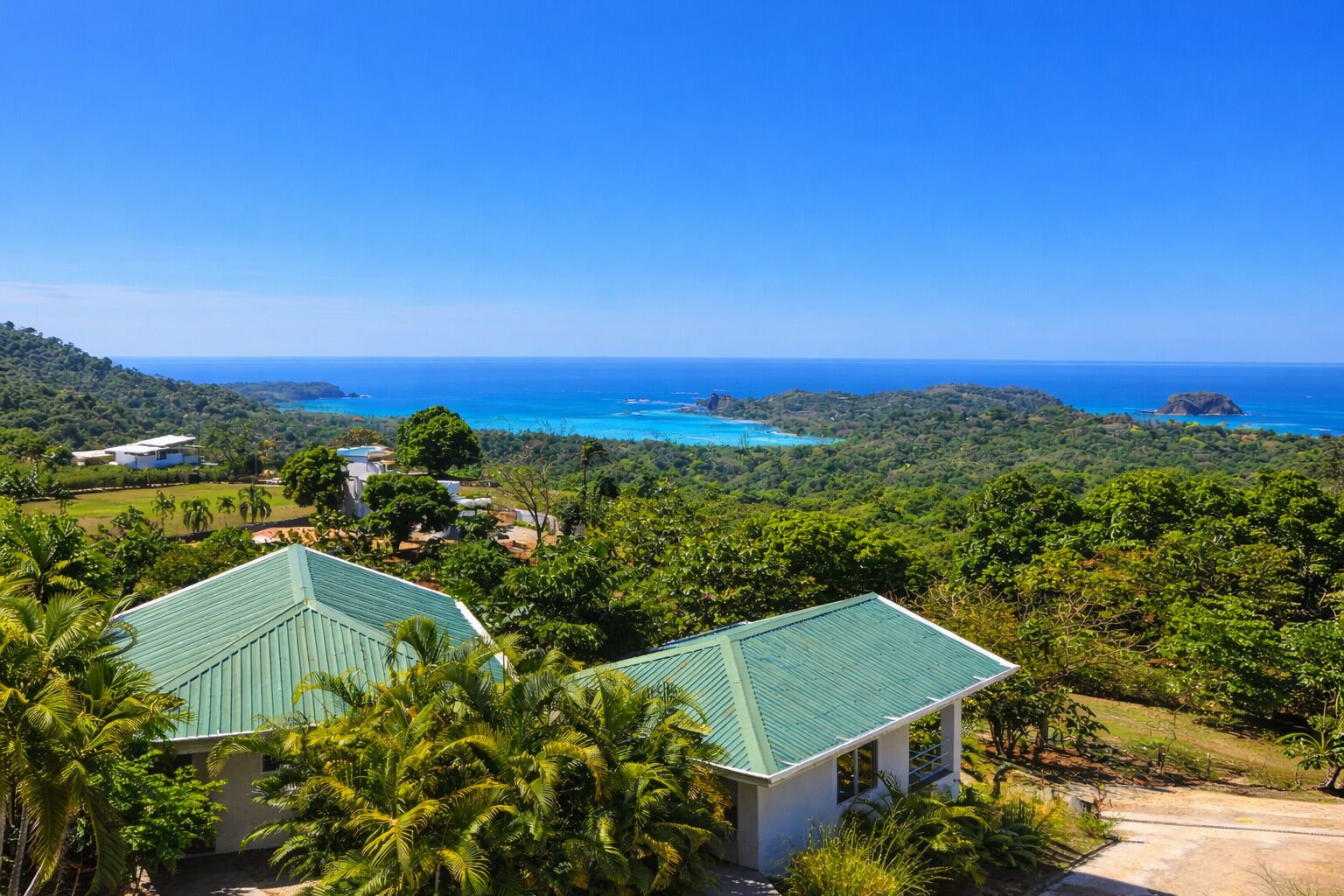 A tropical resort with a green-roofed building surrounded by lush greenery and a view of the ocean.