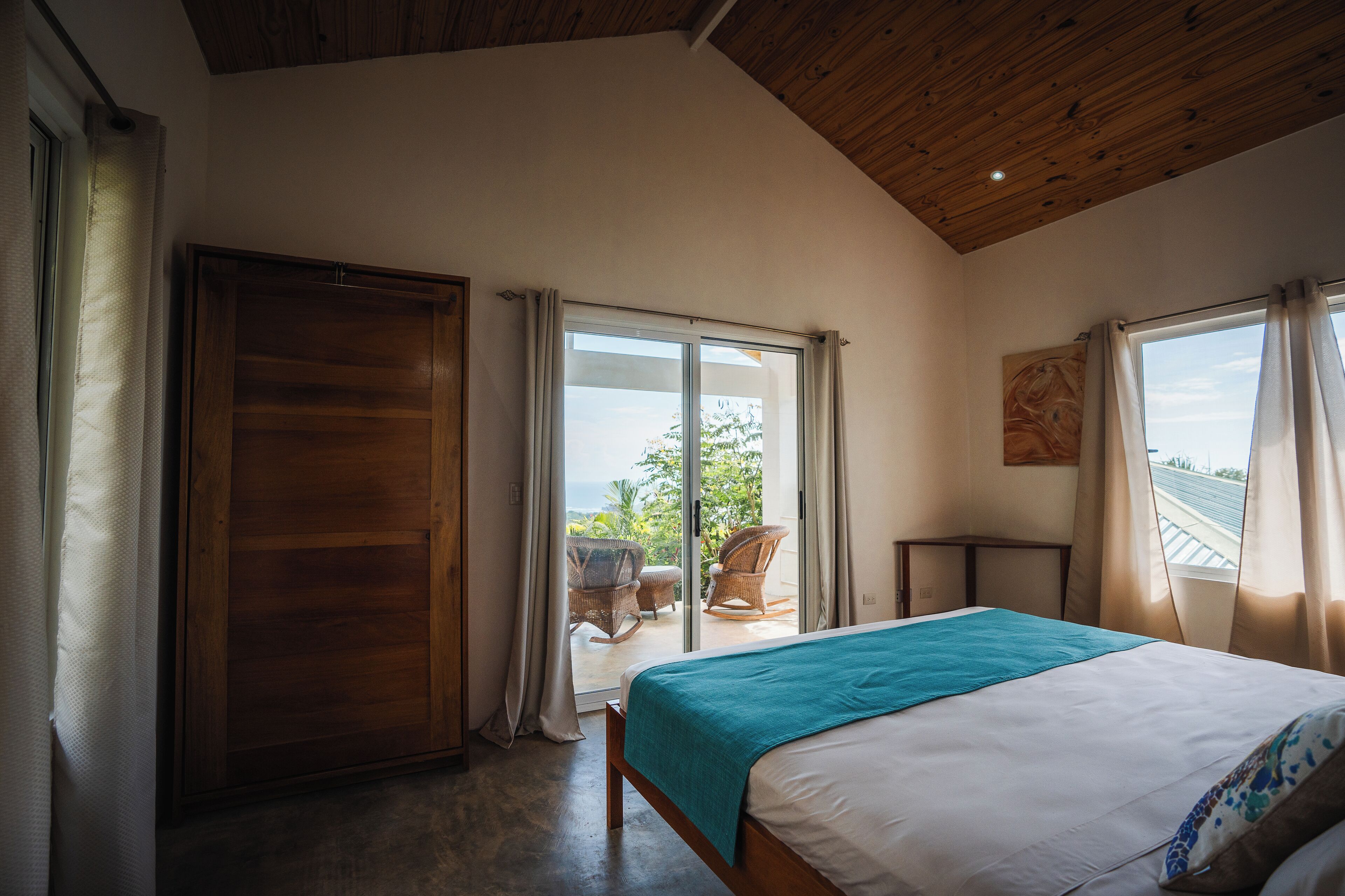 A bedroom with a bed, wooden ceiling, and a view of the outdoors.