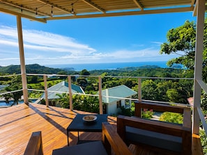Une terrasse en bois avec une table et des chaises, offrant une vue imprenable sur un paysage luxuriant et l’océan.