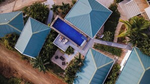 Vista aérea de un resort con varias edificaciones, una piscina central y palmeras alrededor.