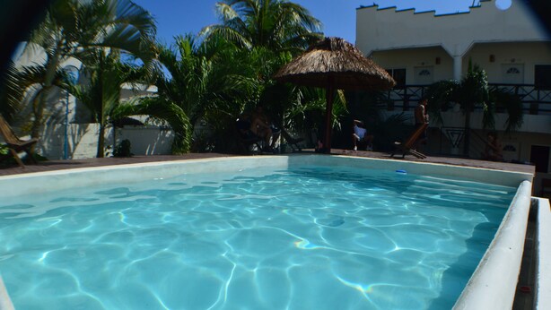Piscina límpida rodeada por palmeiras e uma estrutura com telhado de palha.