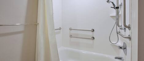 Une salle de bain blanche avec une baignoire, des barres d’appui et une pomme de douche.