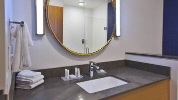 A modern bathroom with a round mirror, a sink, and neatly stacked towels.