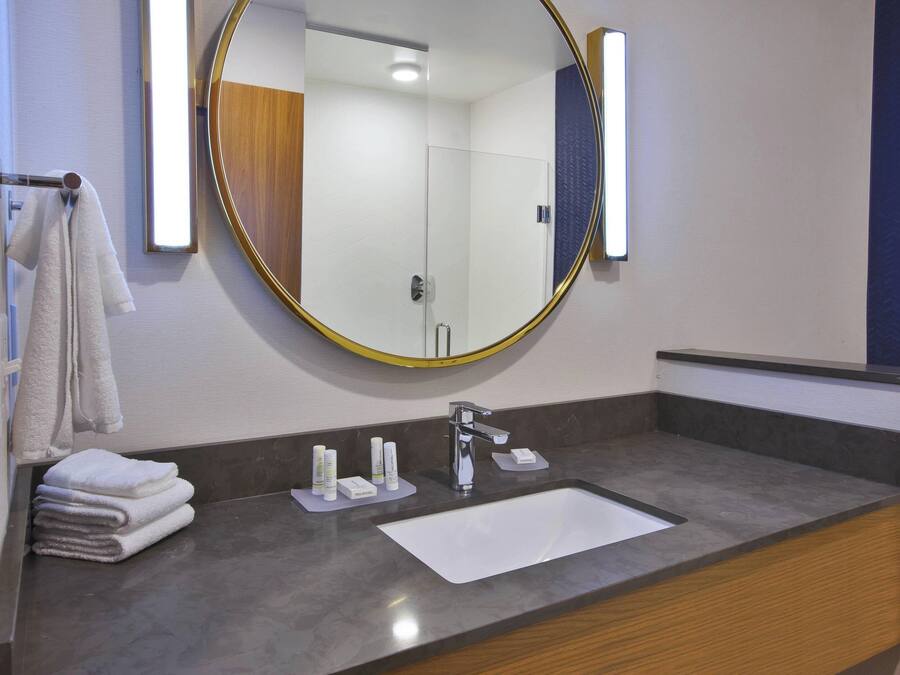 A modern bathroom with a round mirror, a sink, and neatly stacked towels.