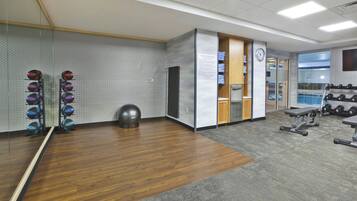 A gym with exercise equipment, a mirrored wall, and a clock.