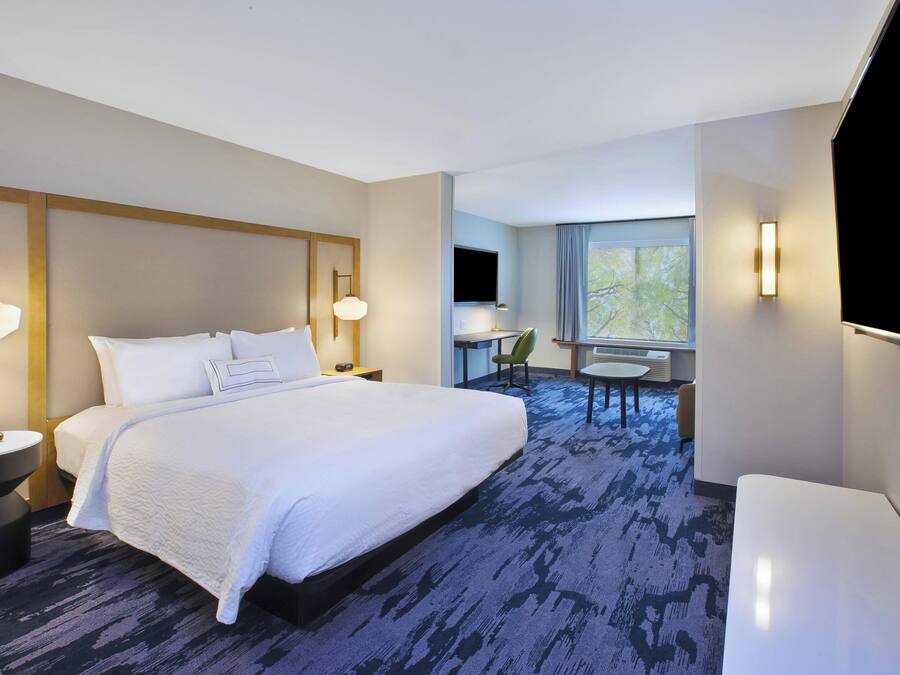 Ein Hotelzimmer mit einem großen Bett, Nachttischen, einem Schreibtisch, einem Sessel und einem Fernseher, sowie einem Fenster mit Blick.