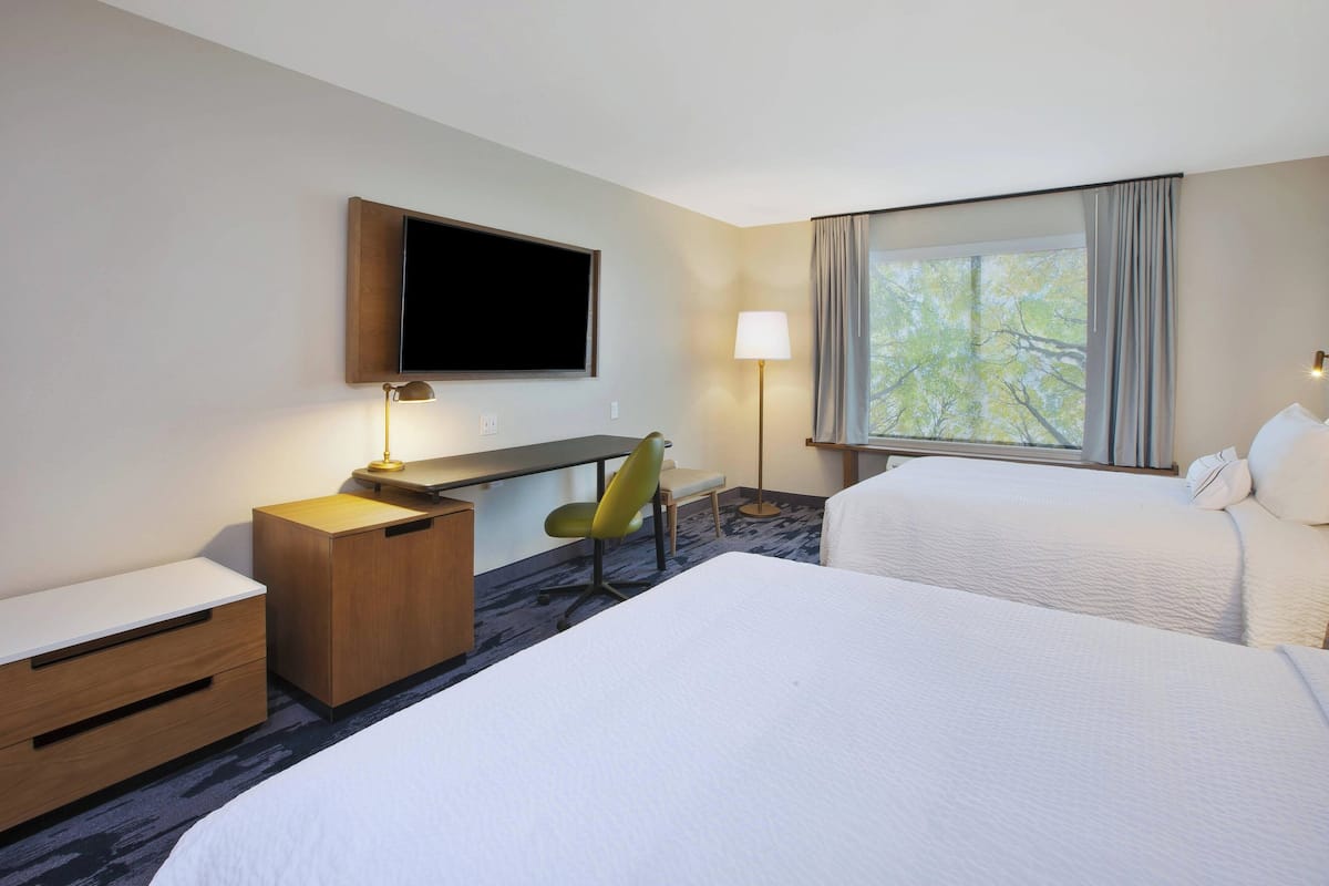 A hotel room with a bed, a desk, a chair, a TV, and a window with curtains.