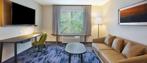 Habitación de hotel con escritorio, silla, sofá, televisión, ventana con cortinas y una lámpara.