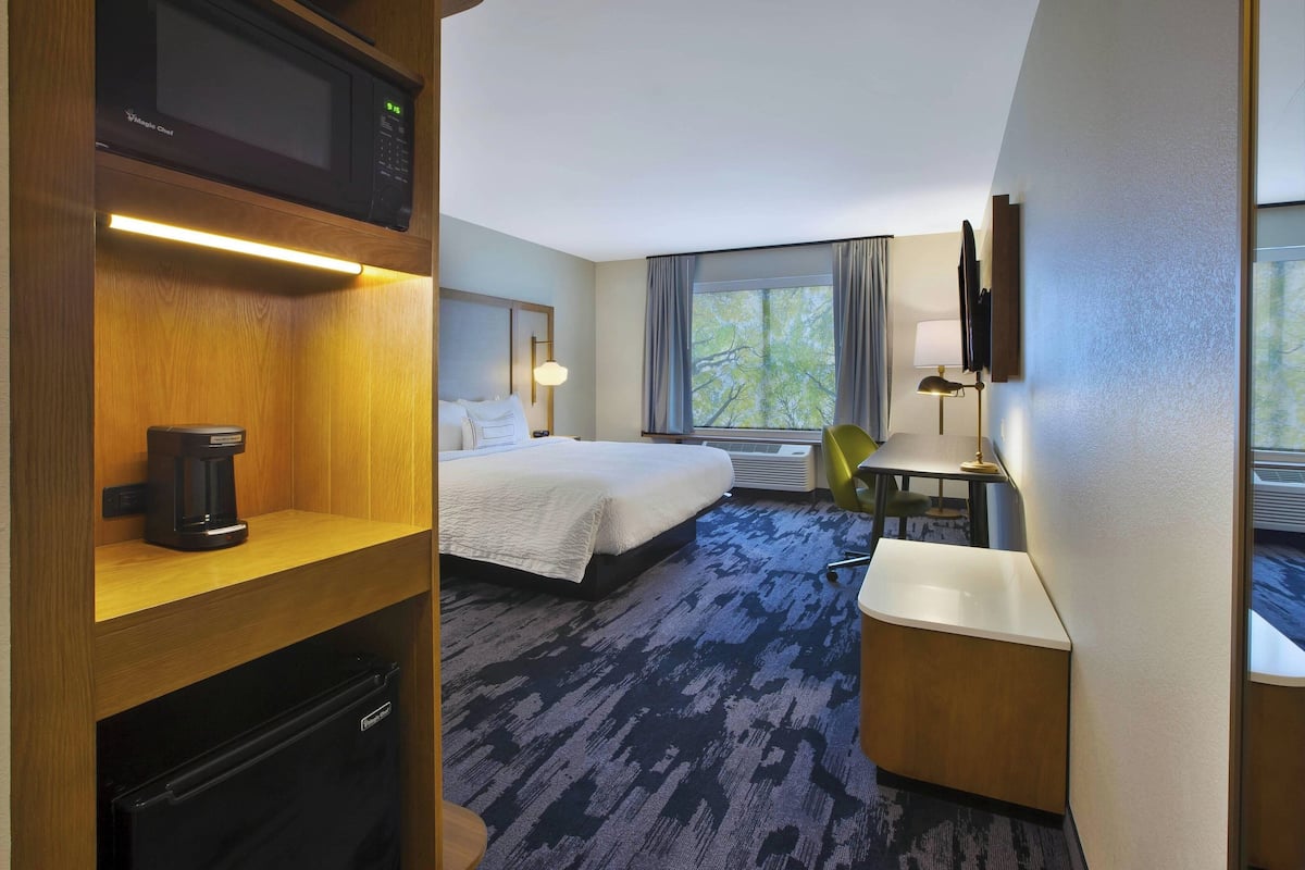 A hotel room with a bed, a desk, a microwave, a coffee maker, and a TV.