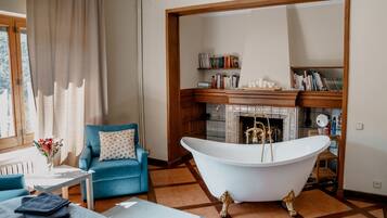 Una habitación con un sillón azul, una bañera blanca, una chimenea y una estantería.