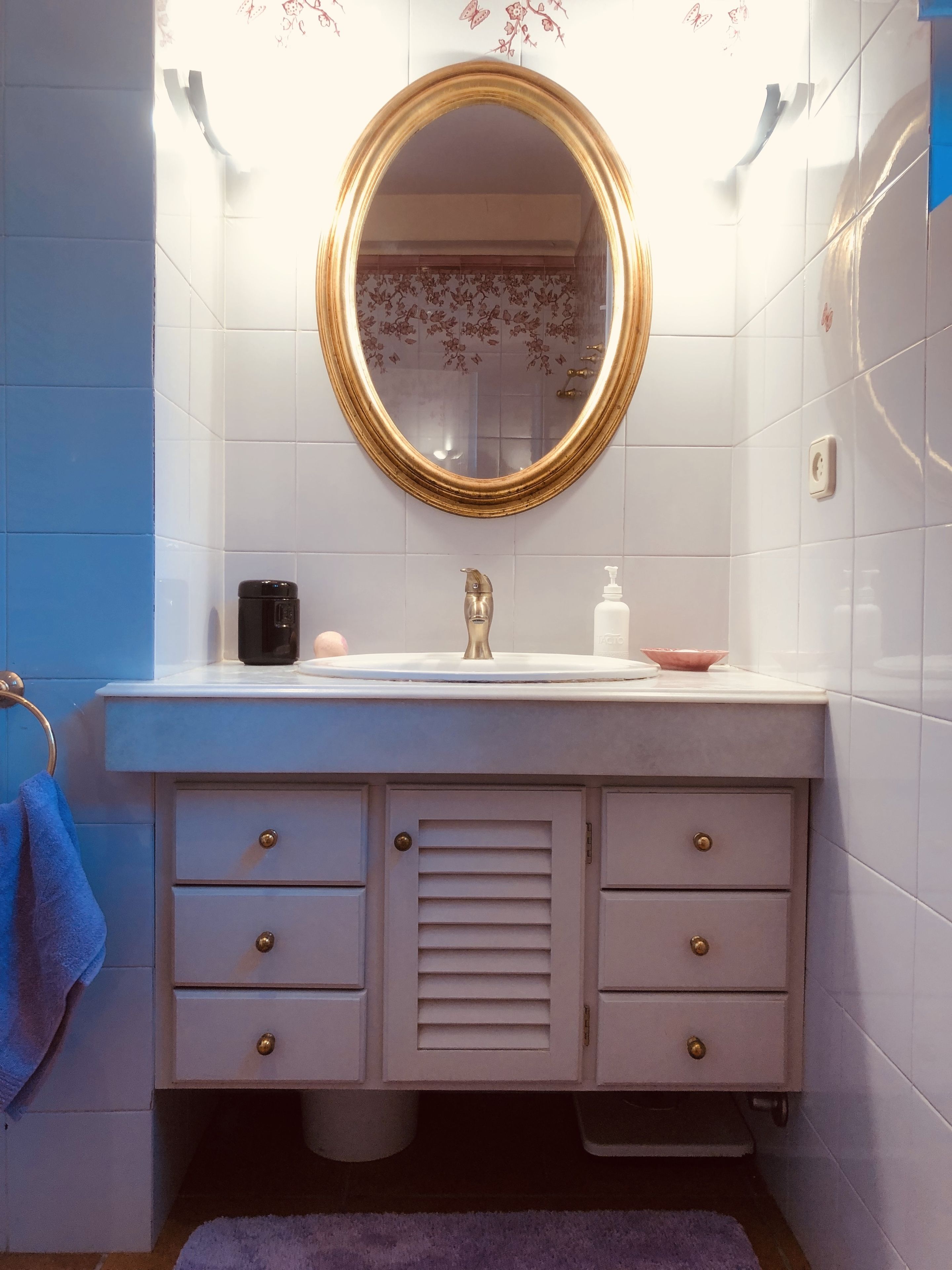 A bathroom with a white vanity, a gold-framed mirror, and a blue towel.