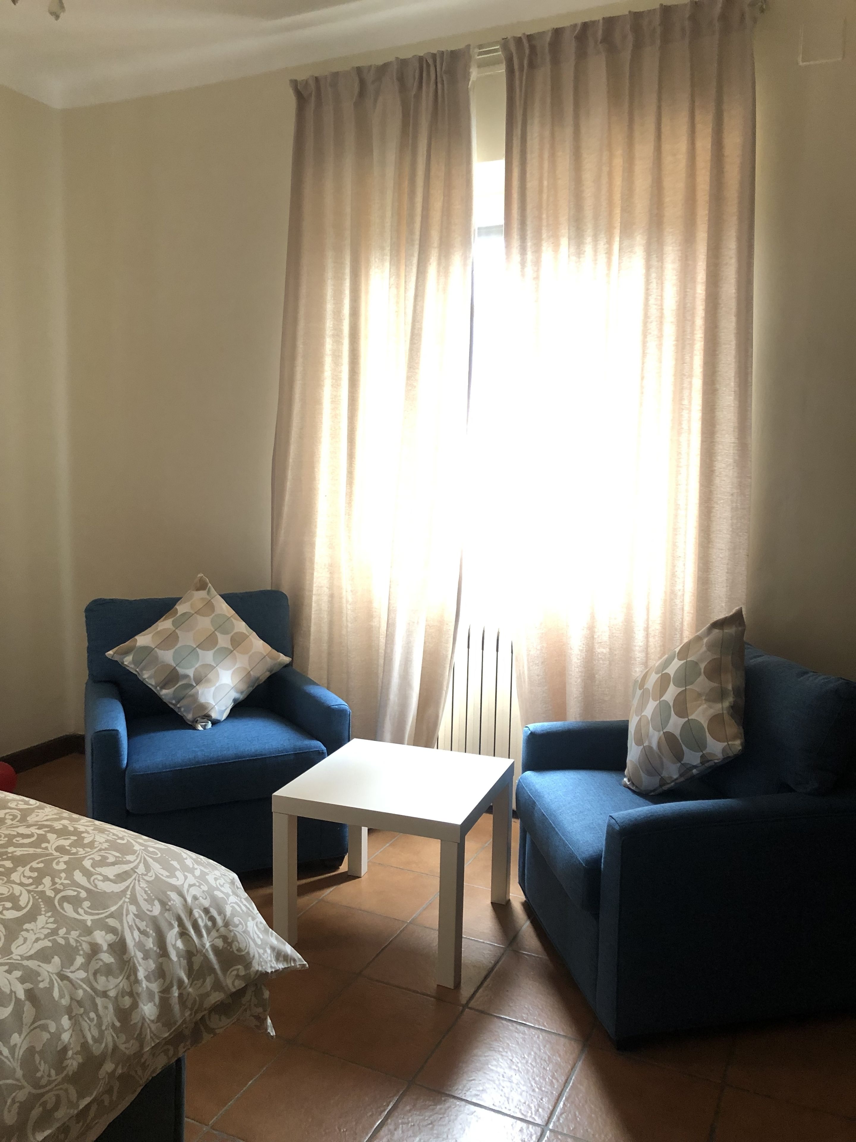 Una sala de estar con dos sofás azules, una mesa de centro blanca y una colcha estampada.