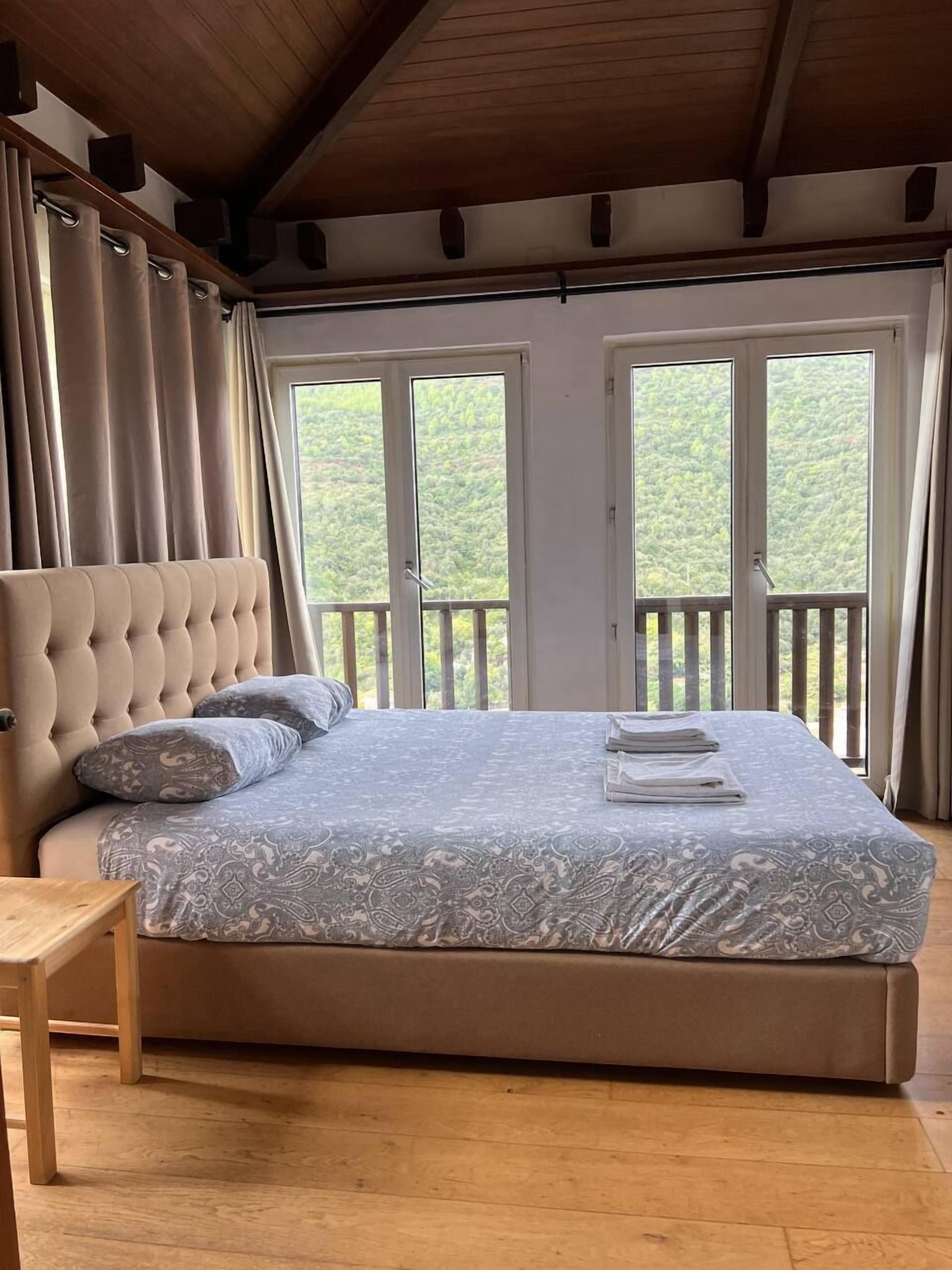 Un dormitorio con una cama grande, un banco de madera y un balcón con cortinas.