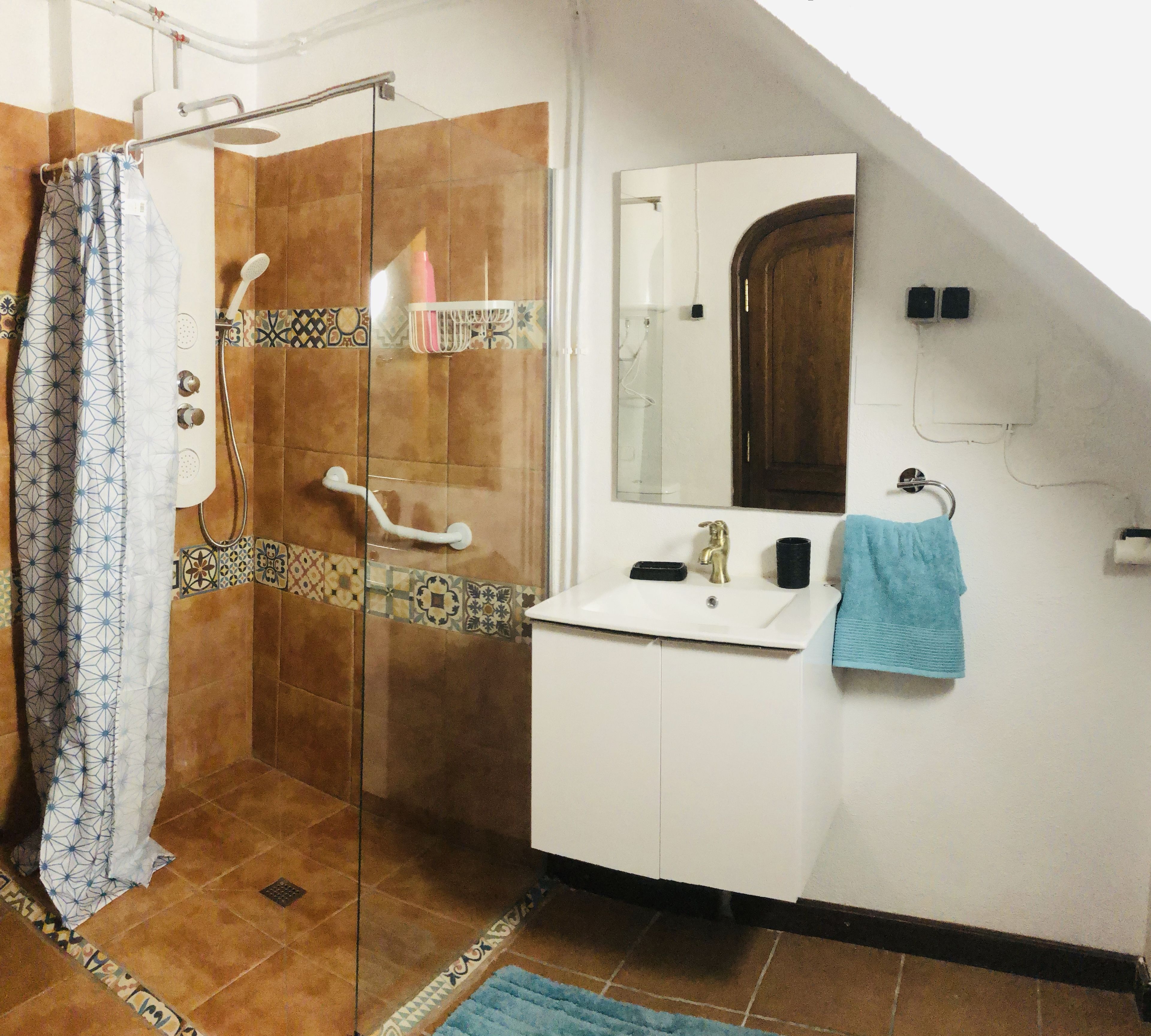 Un baño con cabina de ducha de vidrio, un lavabo blanco, un espejo y una toalla azul.
