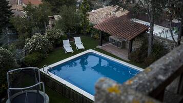 Una piscina con dos sillas de descanso, rodeada de follaje y un edificio de piedra con tejado de baldosas.