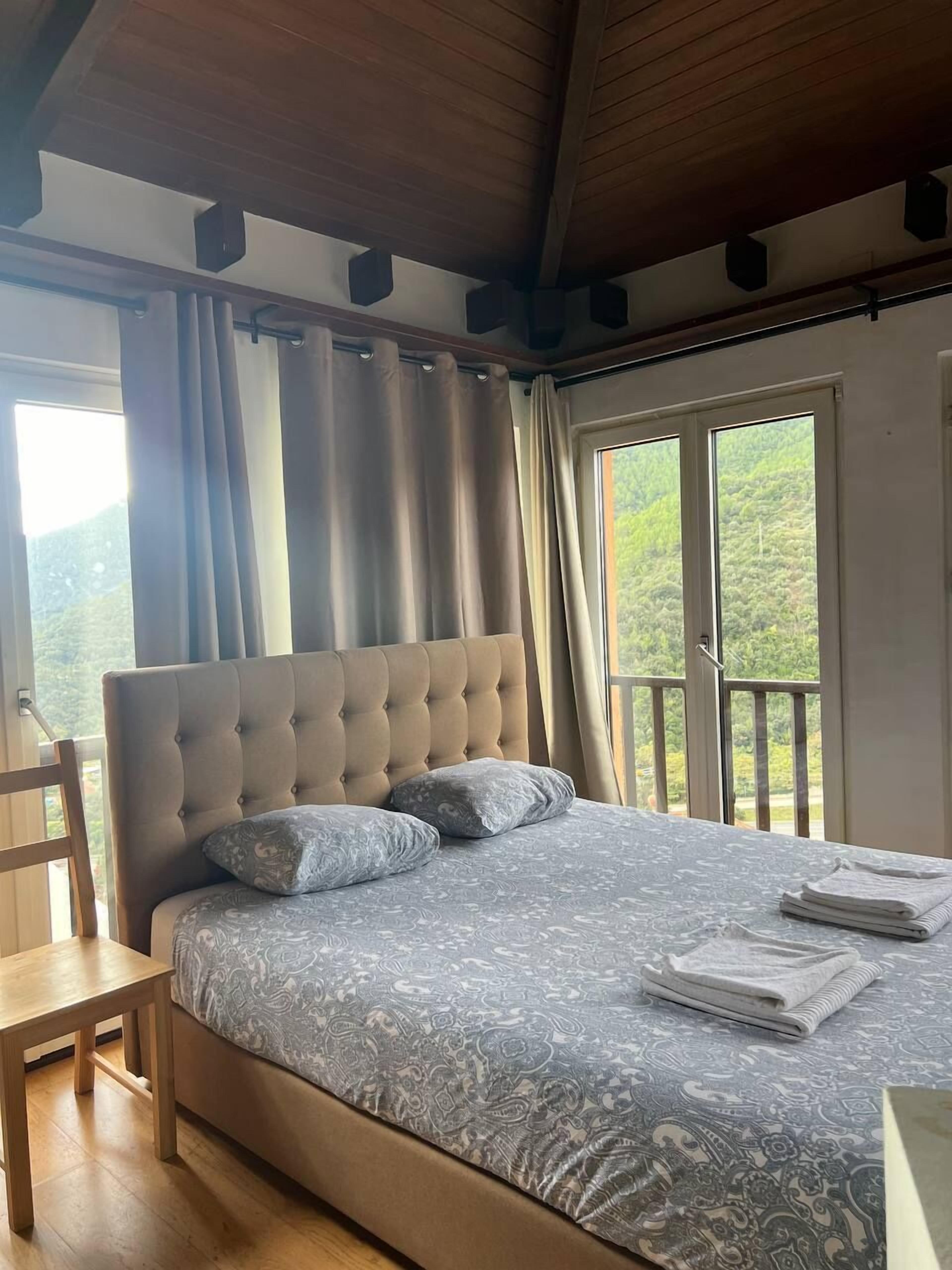 Un dormitorio con una cama grande, una silla de madera y un balcón con vistas a la vegetación.