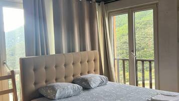 Un dormitorio con una cama grande, una silla de madera y un balcón con vistas a la vegetación.