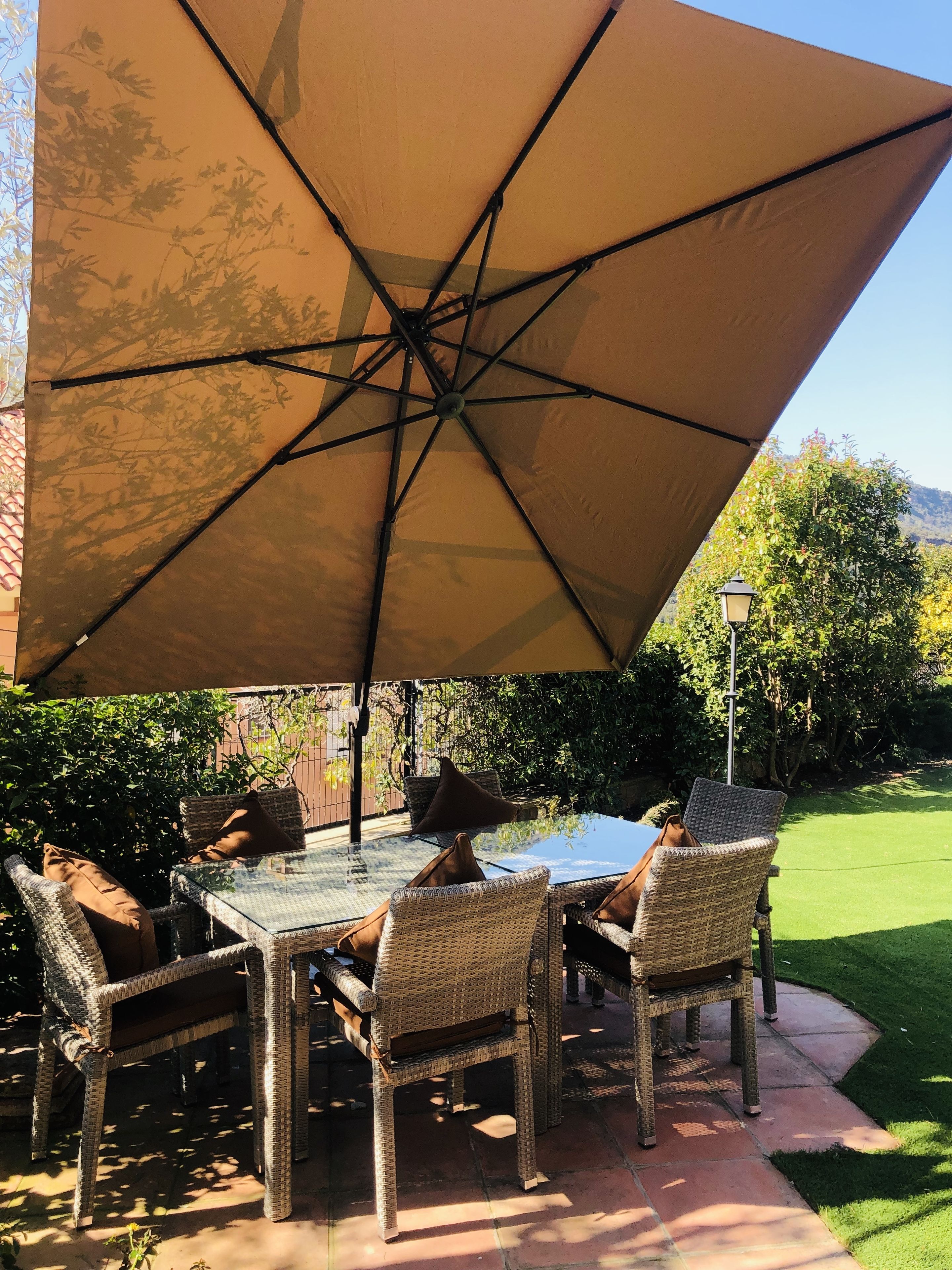 Une terrasse extérieure avec une table en verre et des chaises en osier, protégée du soleil par un grand parasol.
