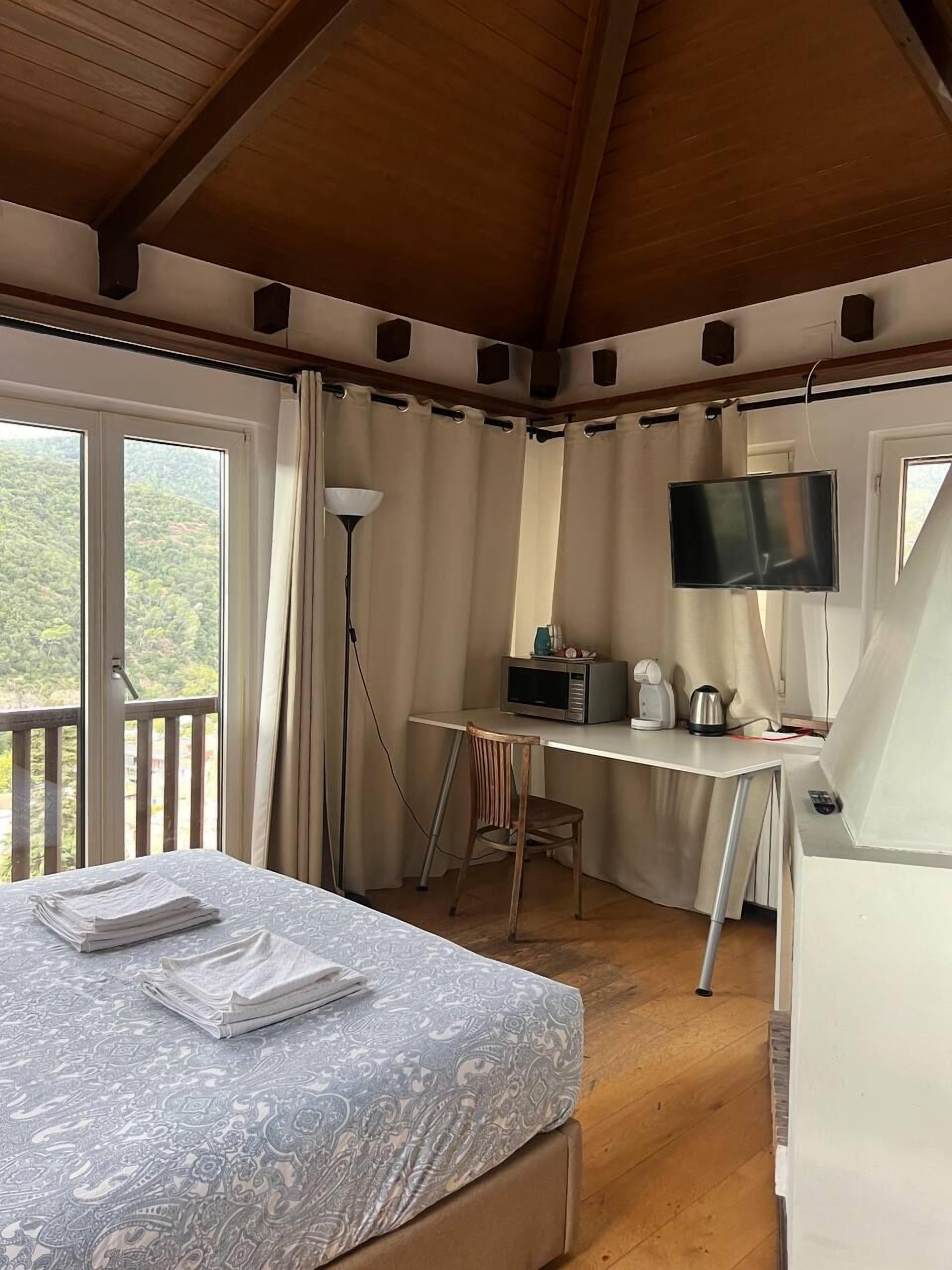Une pièce comprenant un lit, un bureau, une chaise, un téléviseur et une fenêtre avec des rideaux.