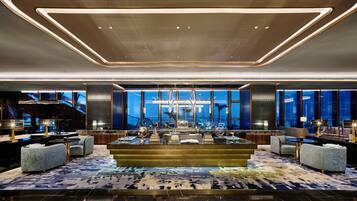A modern lobby with a central bar, seating areas, and large windows offering city views.