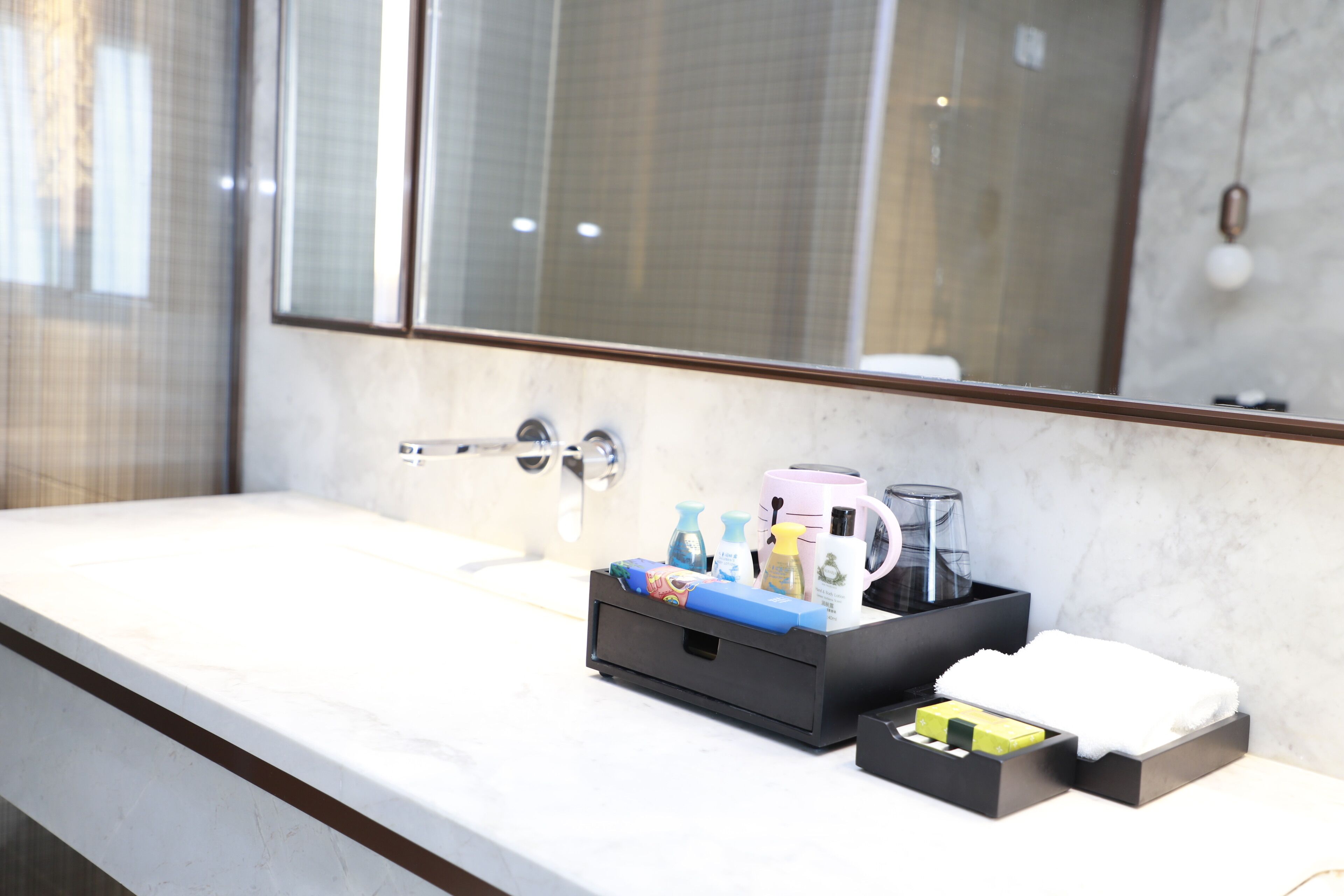 A modern bathroom with a marble countertop, a black storage box with toiletries, and a large mirror.