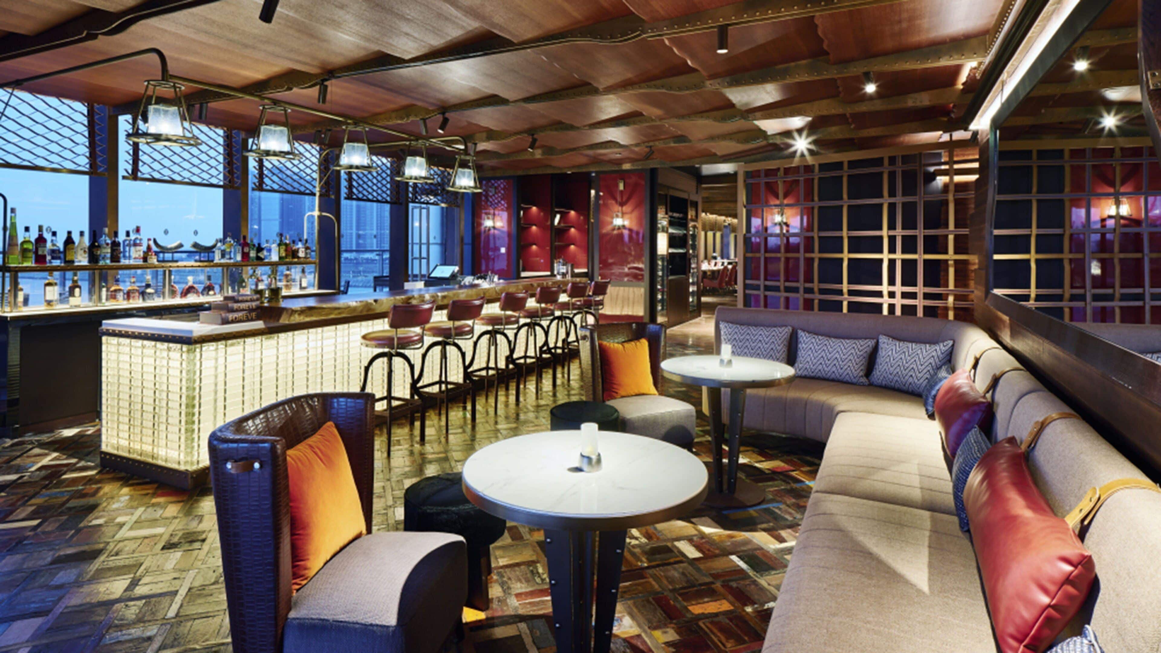 A bar area with a long counter, multiple chairs, and a sofa.