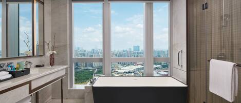 A modern bathroom with a large bathtub, a vanity with a mirror, and a view of a cityscape through large windows.