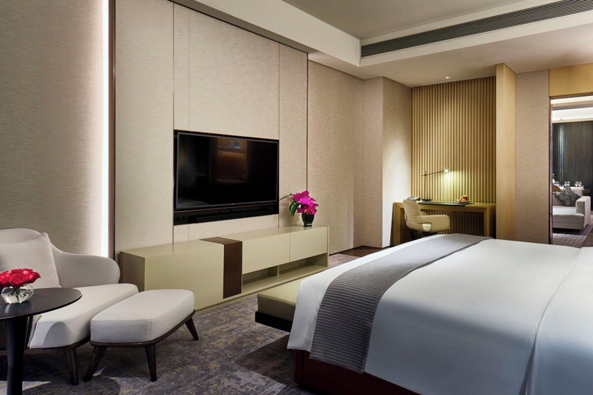 Una habitación de hotel con cama, televisor, escritorio, silla y una mesita con un florero.