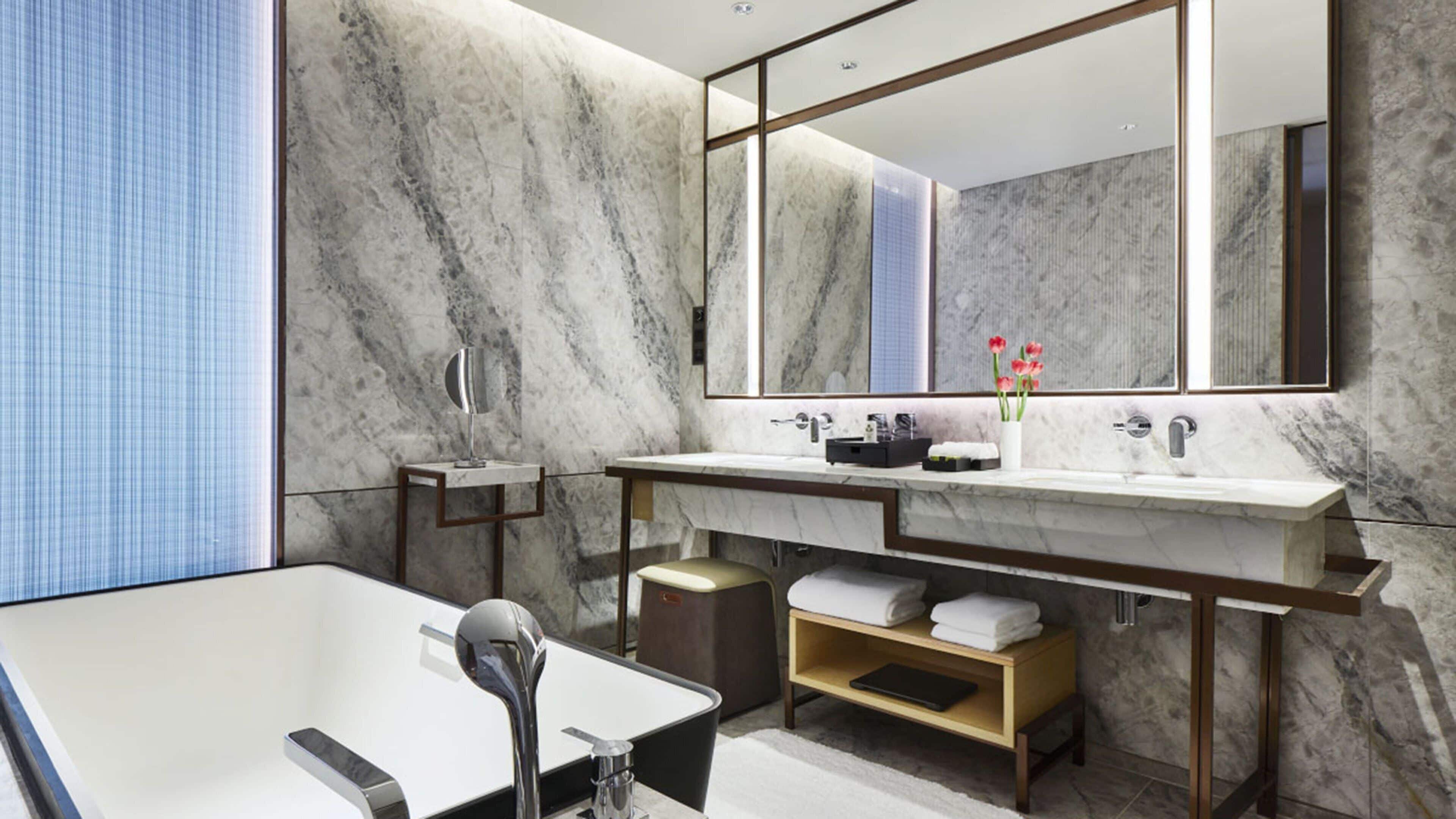 Une salle de bain moderne avec un grand miroir, deux lavabos, une baignoire et des murs en marbre.