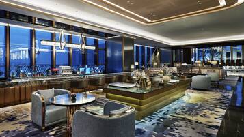 A modern hotel lobby with a bar area, seating, and large windows offering city views.