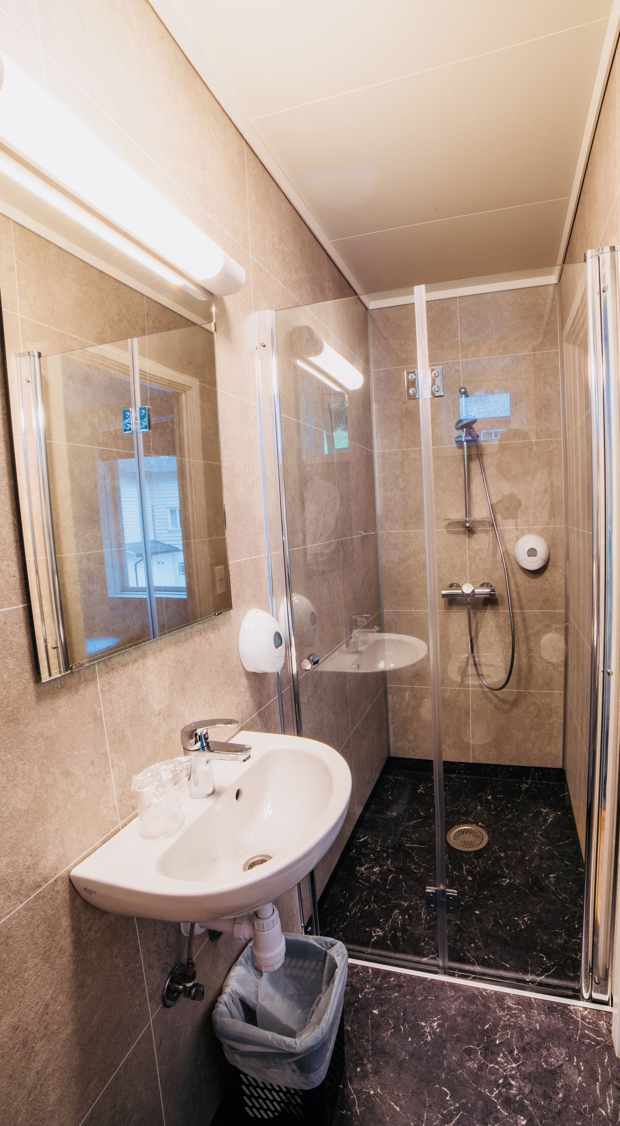 Een moderne badkamer met een douchecabine van glas, een wastafel met een prullenbak en een spiegel.