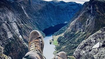 Una persona sentada con las piernas cruzadas, contemplando un valle con un lago y montañas al fondo.