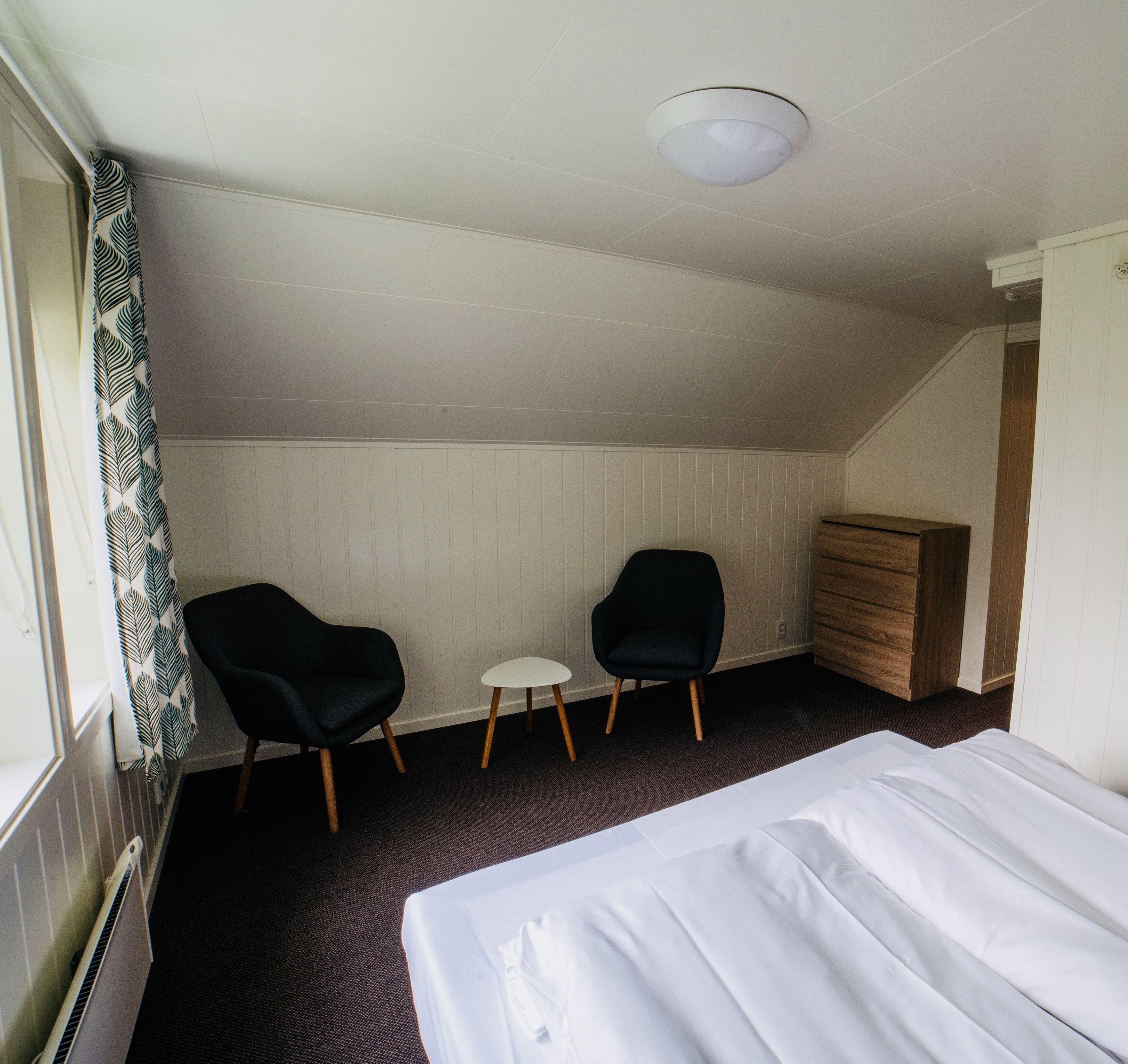A hotel room with a bed, two chairs, a small table, and a dresser.