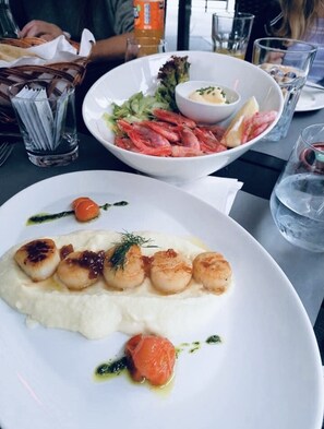 Une table à manger avec une assiette de coquilles Saint-Jacques et un saladier de salade de crevettes.
